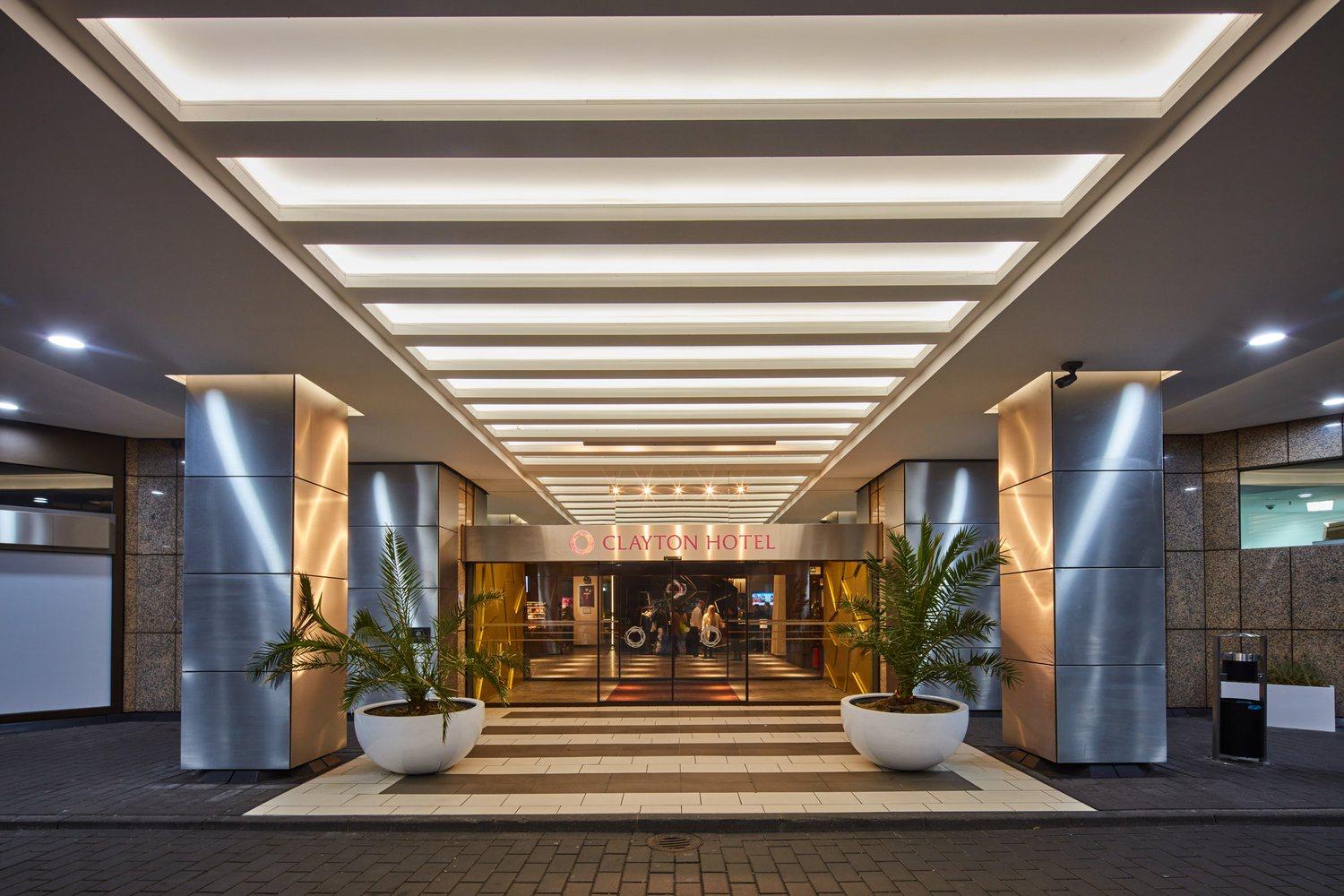 Überdachter Eingang des Clayton Hotel Düsseldorf mit Glastüren und zwei bepflanzten Kübeln.